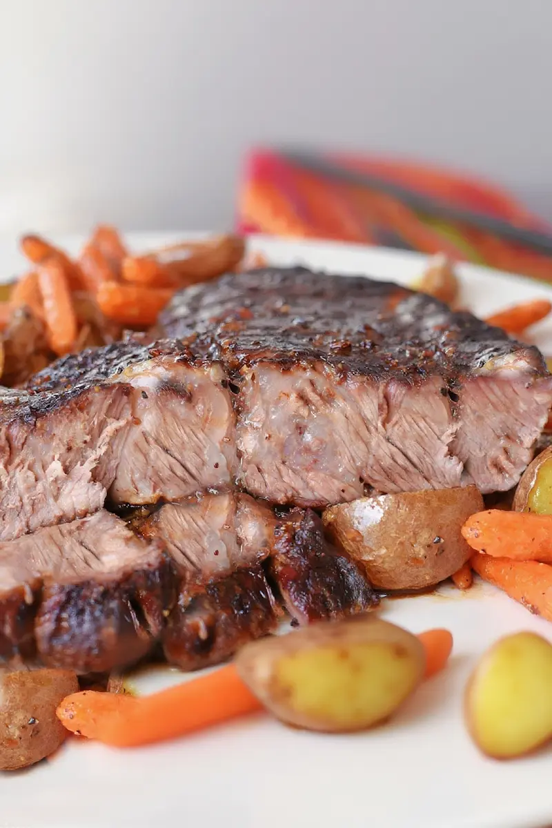 Air fryer chuck roast with crispy exterior, sliced and served with roasted potatoes and carrots
