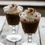 Two glasses of creamy coffee budino topped with whipped cream and cocoa powder, served on a rustic wooden table.