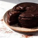 sugarless chocolate truffle cake on a rustic ceramic plate with a clean slice revealing its fudgy interior