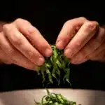 Basil chiffonade being sprinkled over a plated dish, showing thin ribbon-cut fresh basil leaves